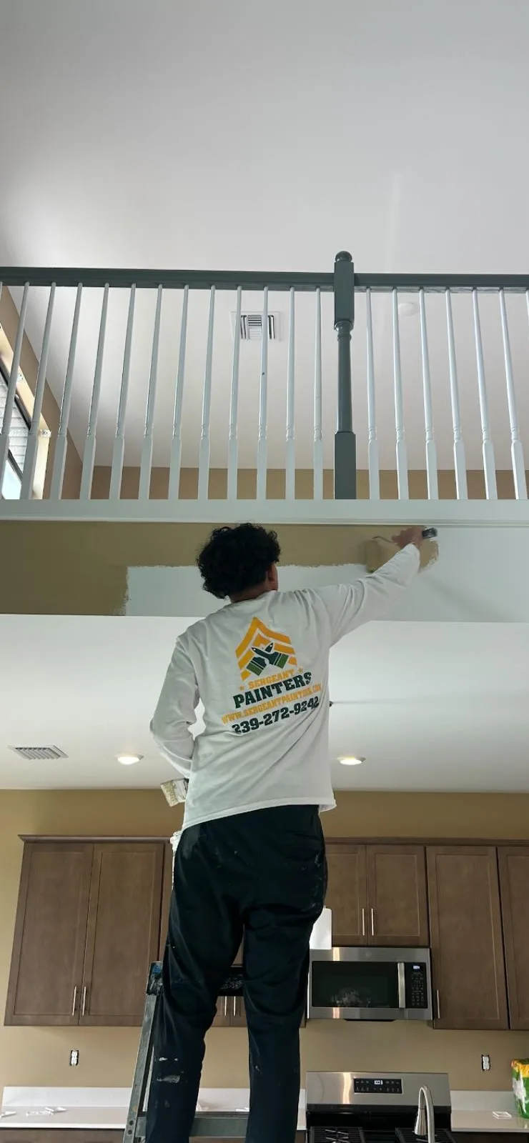 Sergeant Painters crew member in company shirt cutting in a ceiling by hand